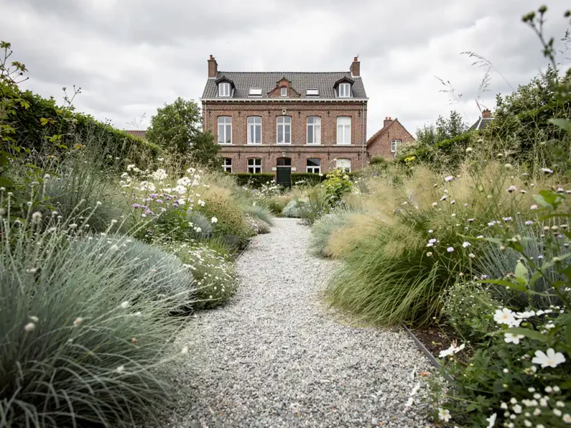 Naturalistische siertuin in volle bloei met siergras en vaste planten langs grindpad naar klassieke bakstenen herenwoning.