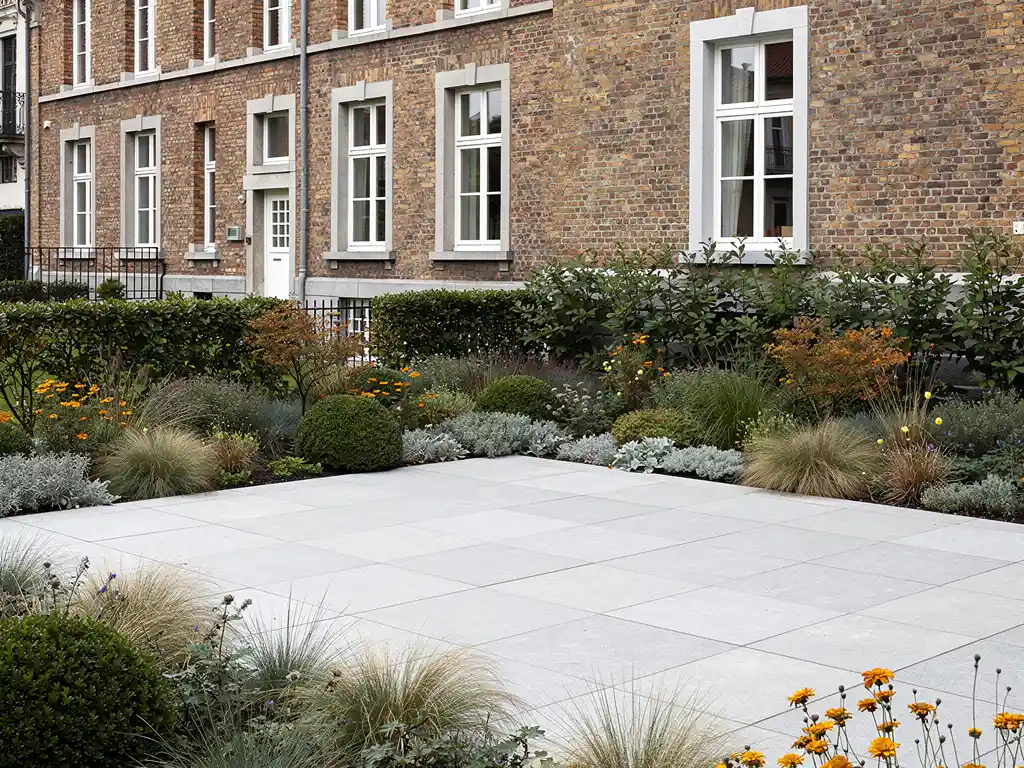 Strak lichtgrijs natuurstenen terras met naturalistische borders van siergras en vaste planten bij klassieke Belgische bakstenen herenwoning.